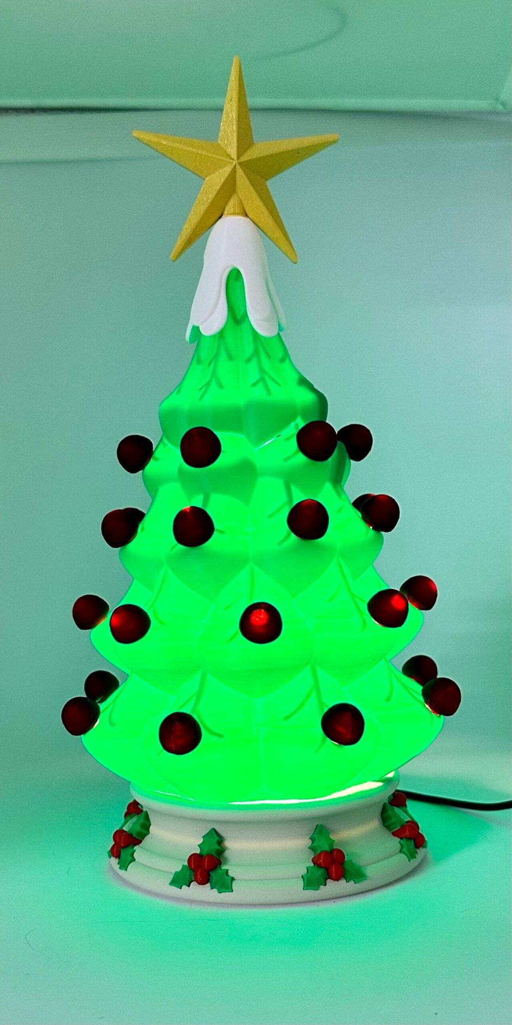 Decorative Christmas tree light with green branches, red ornaments, and a yellow star on top.