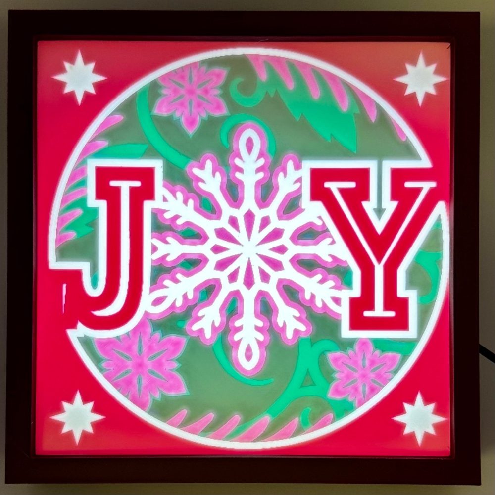 JOY Christmas light decoration featuring a large snowflake and floral design with vibrant backlighting.