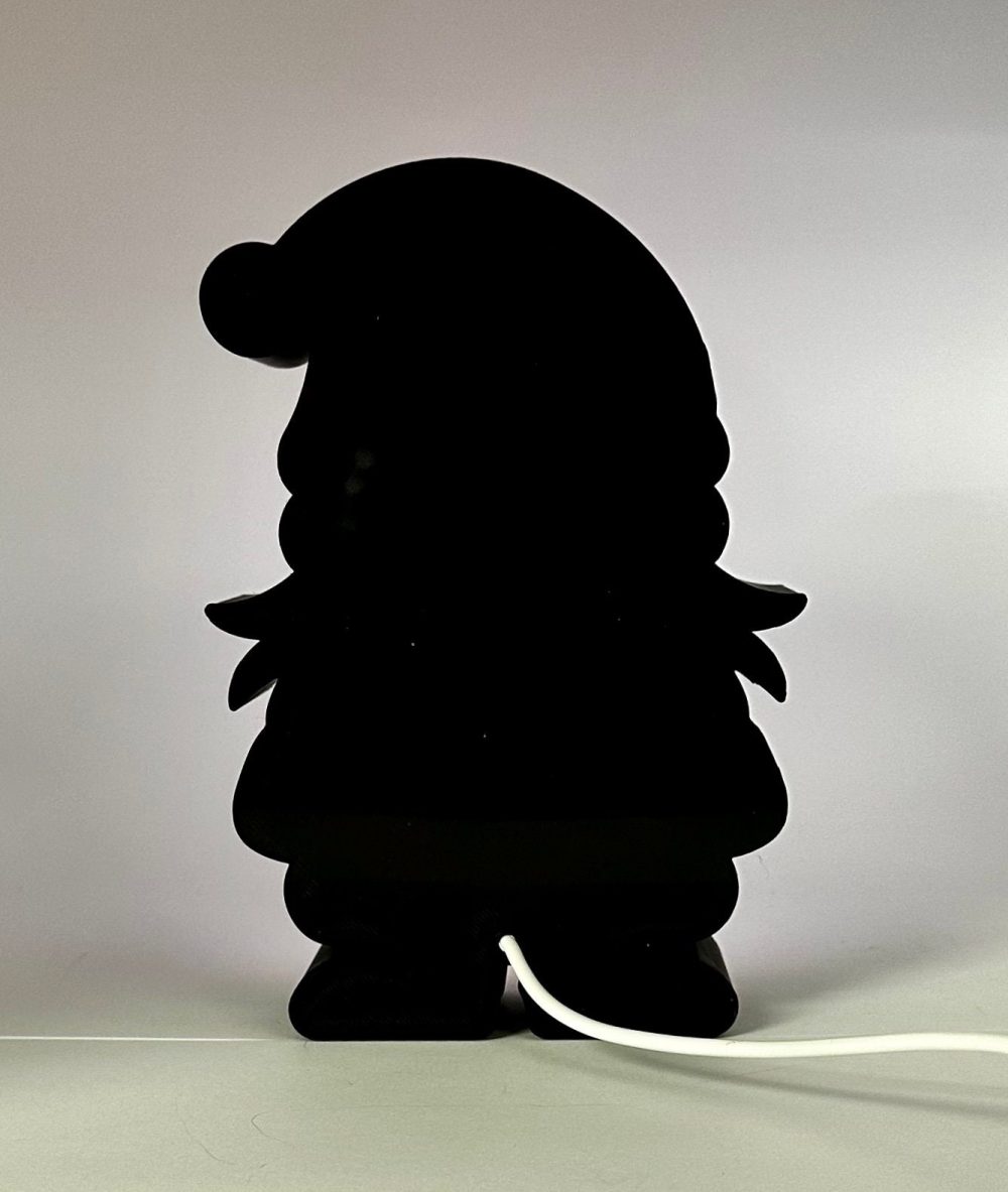 Silhouetted Christmas gnome decoration with lit background and visible power cord.