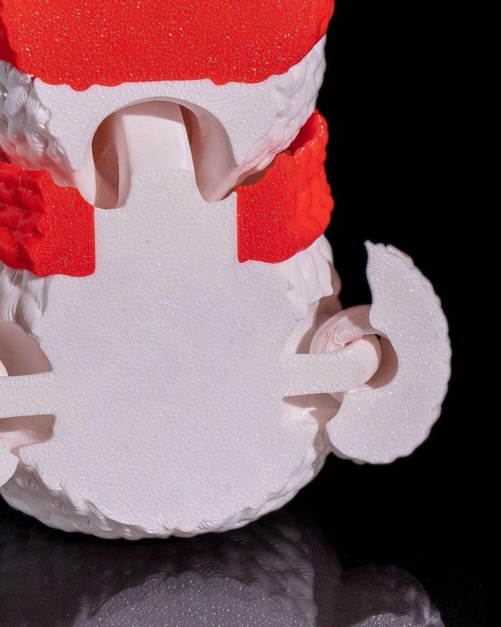 Close-up of the bottom part of a white and red 3D printed snowman decoration with detailed texture on a black background.